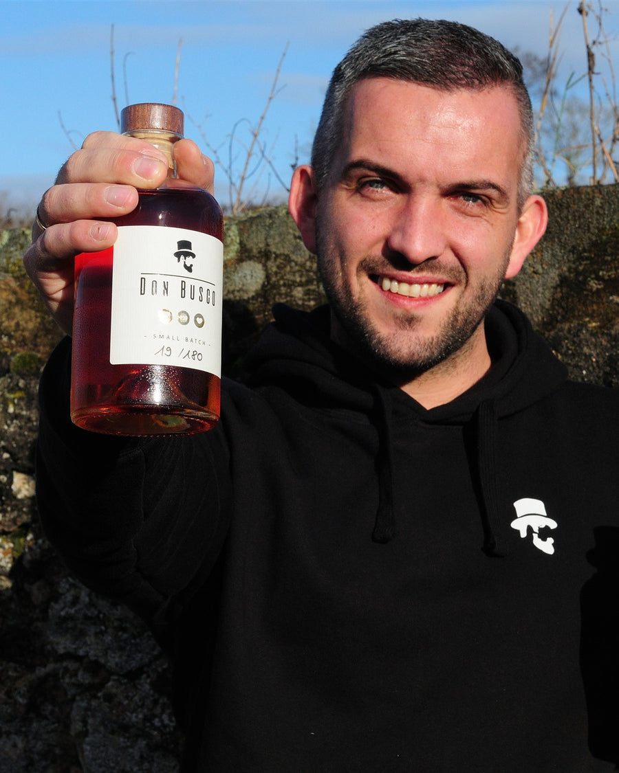 Christian von Don Drinks hält eine Flasche Don Busco vor einer Weinbergsmauer in Rheinhessen
