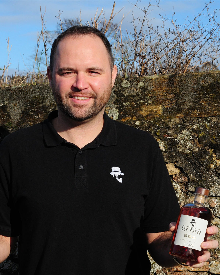 Flo von Don Drinks mit einer Flasche Don Busco vor einer Weinbergsmauer in Rheinhessen